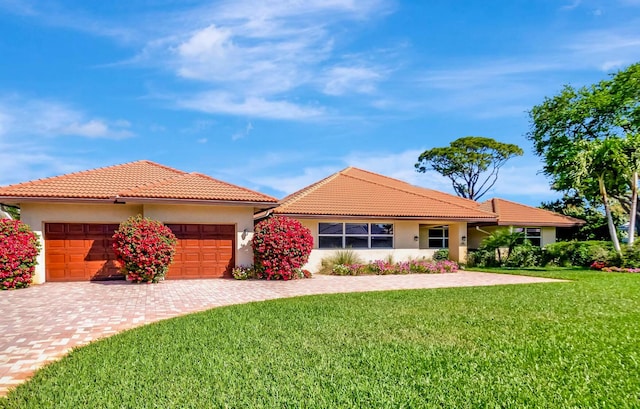 single story home with an attached garage, a tiled roof, a front yard, and stucco siding