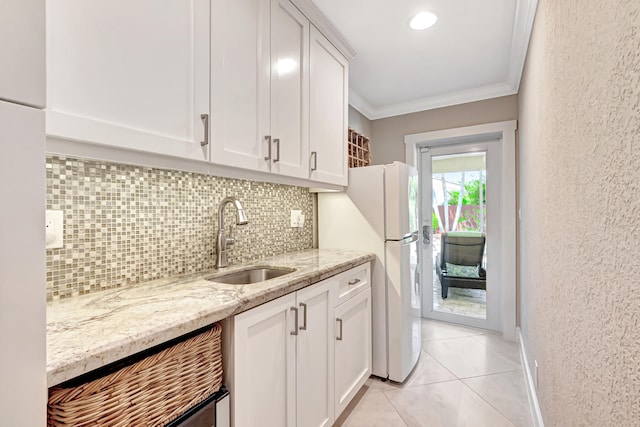 kitchen with white cabinets, white refrigerator, sink, light stone counters, and crown molding