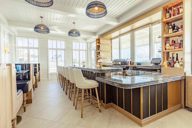 kitchen with kitchen peninsula, a kitchen breakfast bar, dark stone countertops, pendant lighting, and beamed ceiling