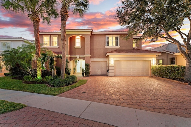 mediterranean / spanish house featuring a garage, a tiled roof, decorative driveway, and stucco siding