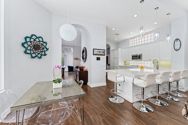 kitchen with dark hardwood / wood-style floors, kitchen peninsula, pendant lighting, decorative backsplash, and white cabinets