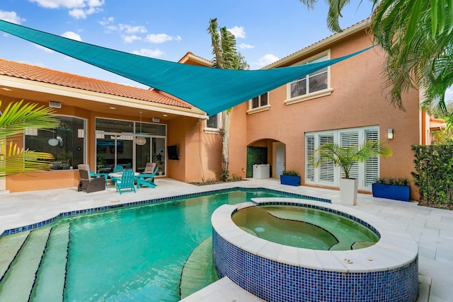 back of house with stucco siding, a pool with connected hot tub, a tile roof, and a patio