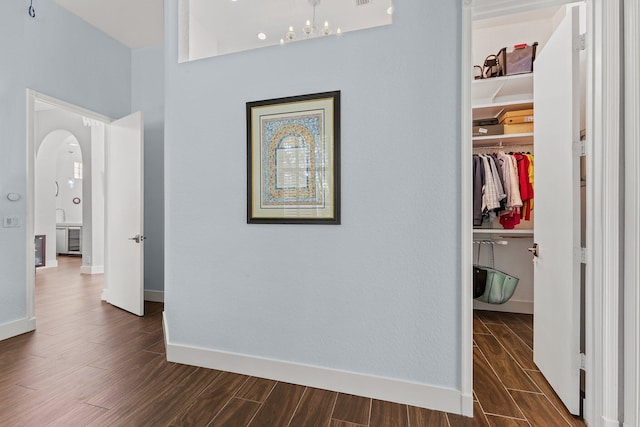 hall featuring arched walkways, wood finish floors, and baseboards