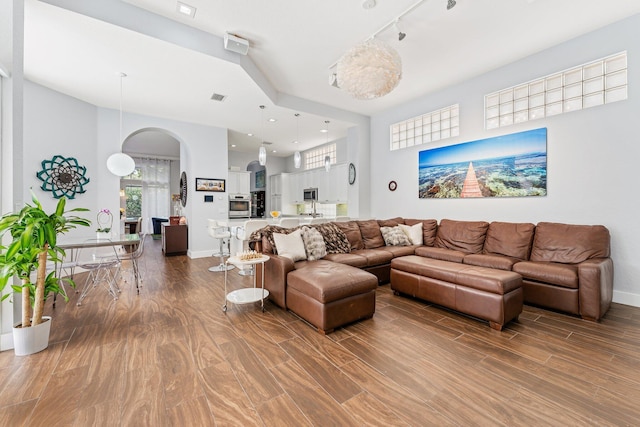 living room with rail lighting, baseboards, arched walkways, and wood finished floors