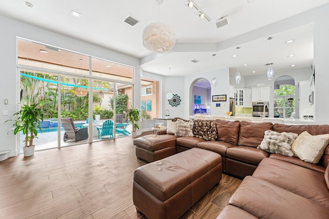 living room with arched walkways, wood finished floors, visible vents, and rail lighting