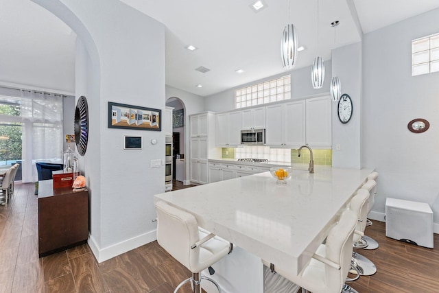 kitchen featuring tasteful backsplash, white cabinets, appliances with stainless steel finishes, light stone countertops, and a sink