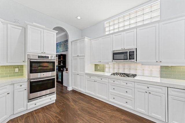 kitchen featuring tasteful backsplash, arched walkways, white cabinets, appliances with stainless steel finishes, and light countertops