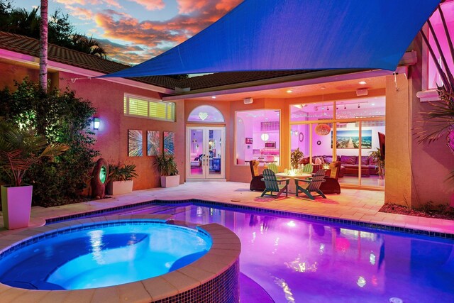 pool at dusk featuring a pool with connected hot tub, a patio, and french doors