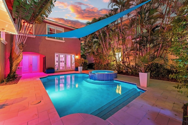 pool at dusk with a patio area and a pool with connected hot tub