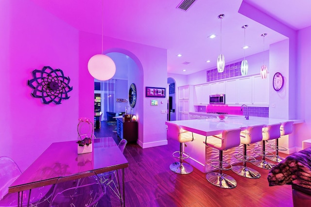 bar with visible vents, arched walkways, stainless steel microwave, dark wood-type flooring, and pendant lighting