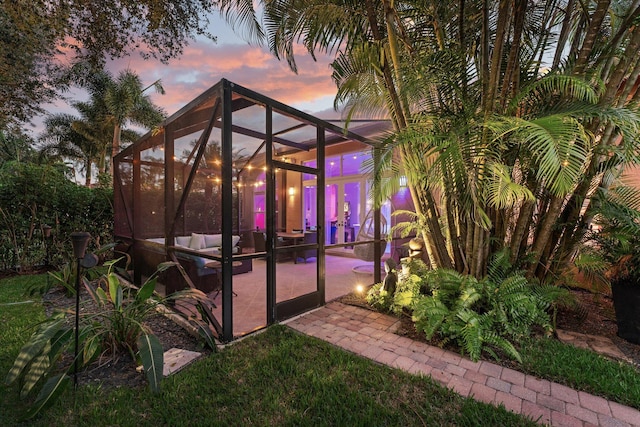 yard at dusk featuring glass enclosure and a patio