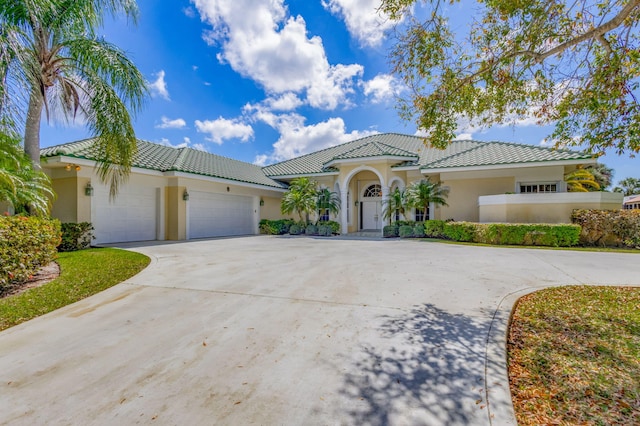 mediterranean / spanish-style house featuring driveway, an attached garage, a tiled roof, and stucco siding