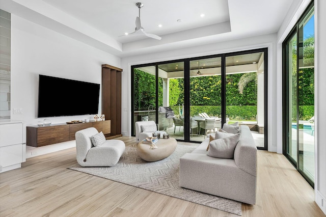 living room with a tray ceiling, ceiling fan, and light wood-type flooring