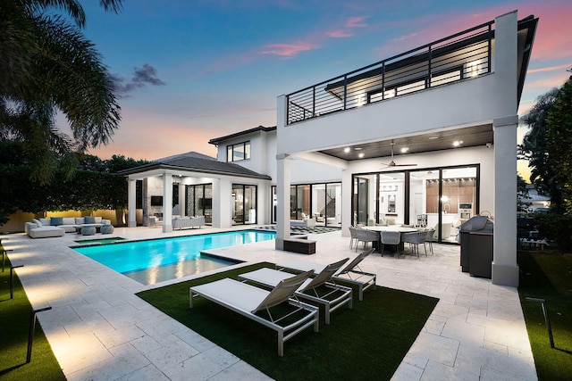 back house at dusk featuring outdoor lounge area, ceiling fan, a balcony, and a patio area