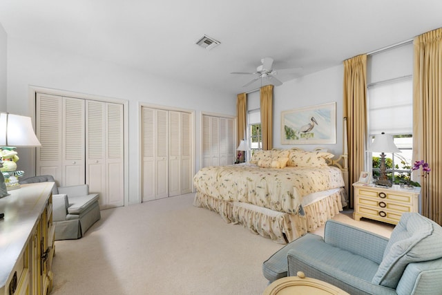 bedroom featuring multiple closets, light colored carpet, and ceiling fan