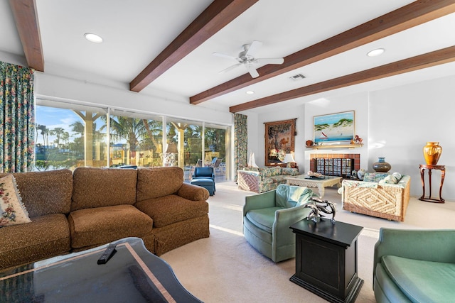 living room with ceiling fan, light colored carpet, beam ceiling, and a tile fireplace