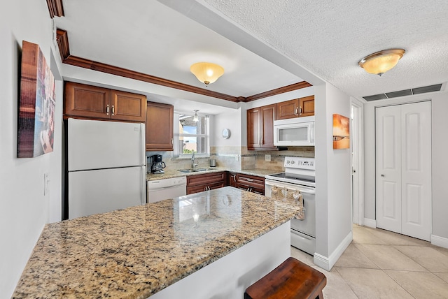 kitchen with white appliances, a breakfast bar, backsplash, sink, and light stone countertops