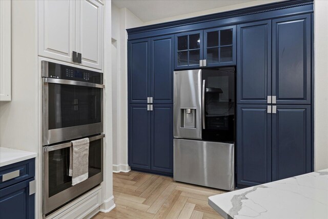 kitchen with appliances with stainless steel finishes, light parquet flooring, blue cabinets, and light stone counters