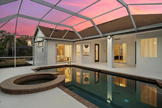 pool at dusk featuring an in ground hot tub, glass enclosure, and a patio area