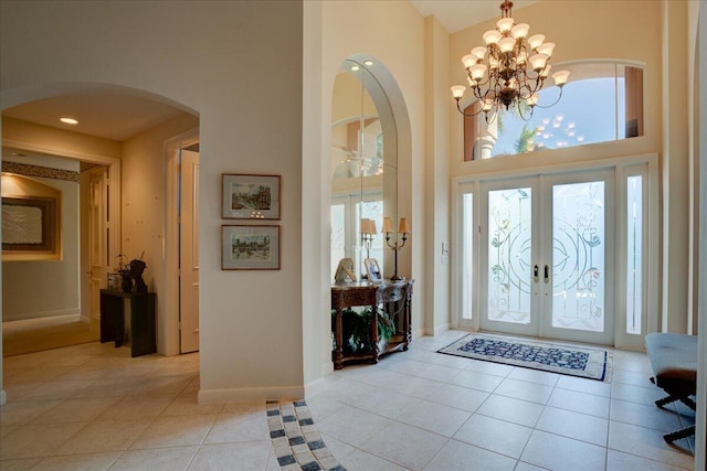 entryway featuring french doors, light tile patterned flooring, a high ceiling, and an inviting chandelier