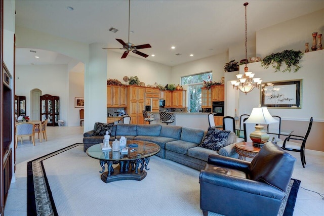 tiled living room with ceiling fan with notable chandelier and a high ceiling