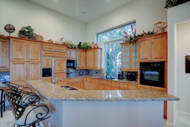 kitchen featuring a kitchen breakfast bar, backsplash, sink, black appliances, and an island with sink