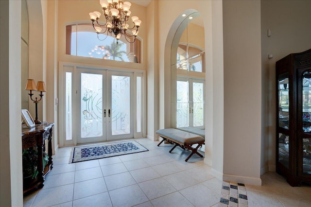 tiled foyer entrance featuring french doors, a towering ceiling, and a chandelier