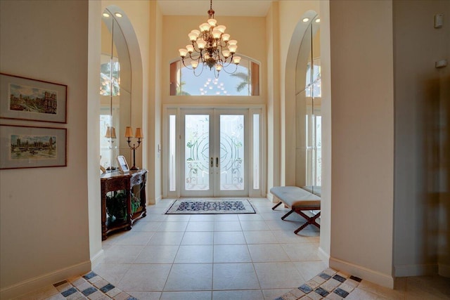 tiled entryway with an inviting chandelier, a towering ceiling, and french doors