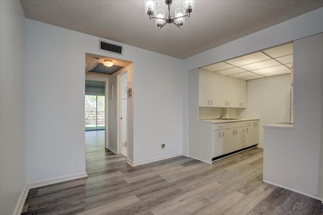 unfurnished dining area with a textured ceiling, light hardwood / wood-style floors, a notable chandelier, and sink