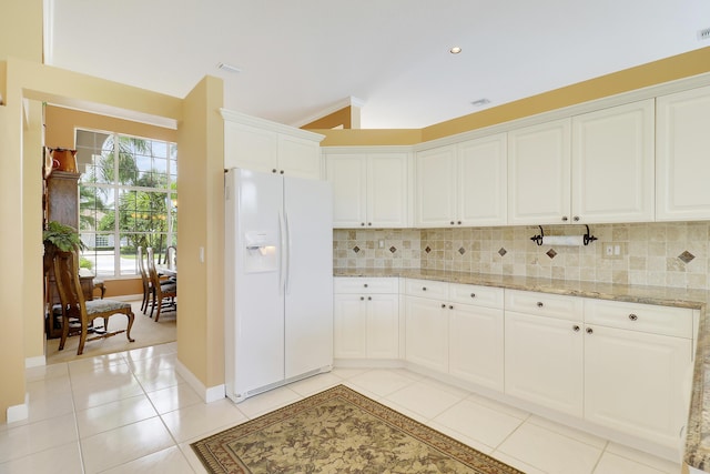 kitchen featuring white cabinetry, decorative backsplash, white refrigerator with ice dispenser, light tile patterned floors, and light stone counters