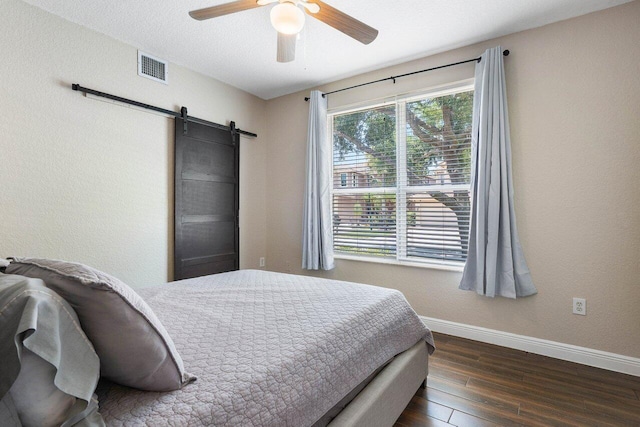 bedroom with ceiling fan, a barn door, and dark hardwood / wood-style flooring