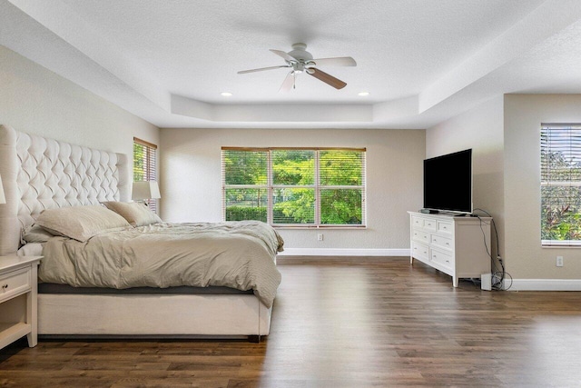 bedroom featuring multiple windows, a tray ceiling, ceiling fan, and dark wood-type flooring