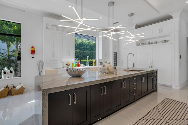 kitchen with light stone counters, ornamental molding, a spacious island, sink, and white cabinets