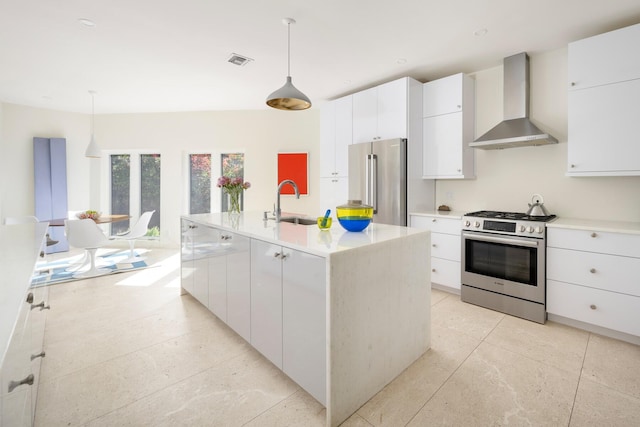 kitchen featuring high quality appliances, a center island with sink, wall chimney exhaust hood, and decorative light fixtures