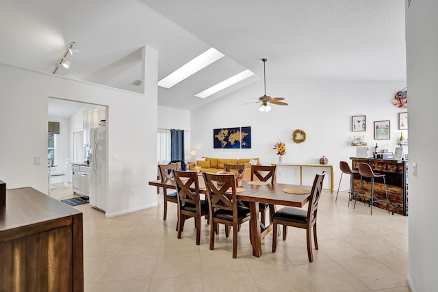 tiled dining area featuring ceiling fan, vaulted ceiling with skylight, and track lighting