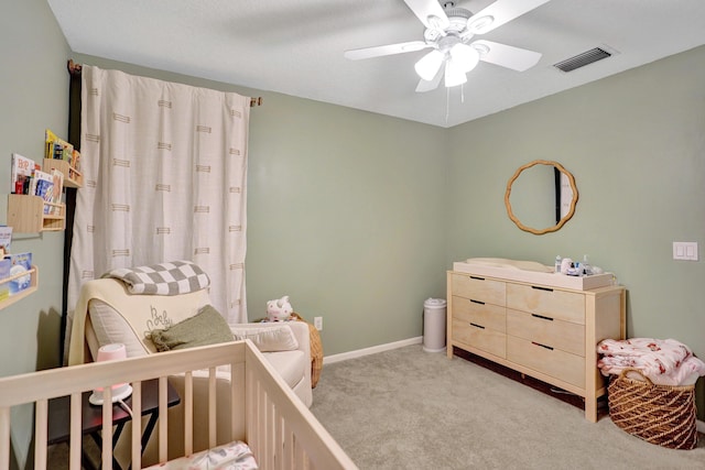 carpeted bedroom with a crib and ceiling fan