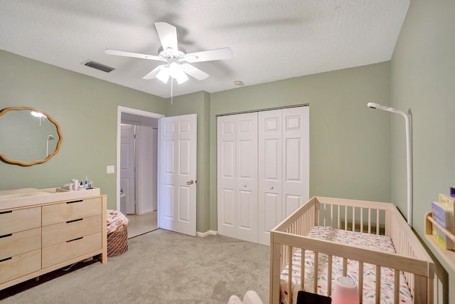 carpeted bedroom featuring a nursery area, ceiling fan, a closet, and a textured ceiling