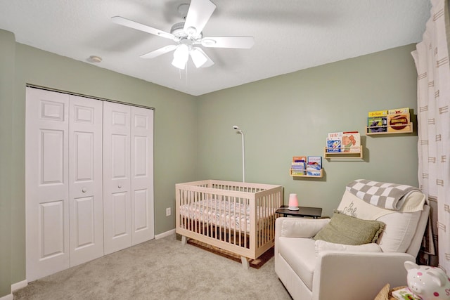 bedroom with ceiling fan, a textured ceiling, light colored carpet, a crib, and a closet