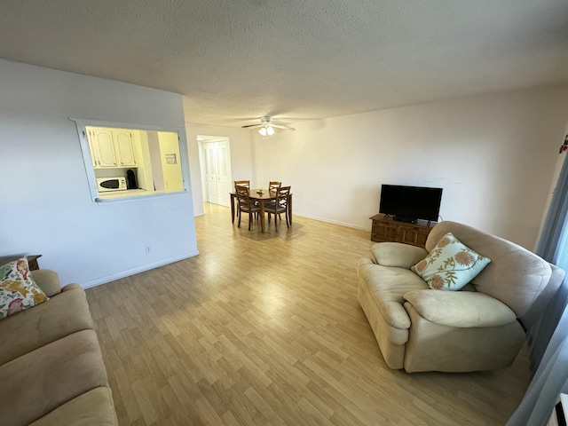 living room featuring a textured ceiling, light wood-type flooring, and ceiling fan