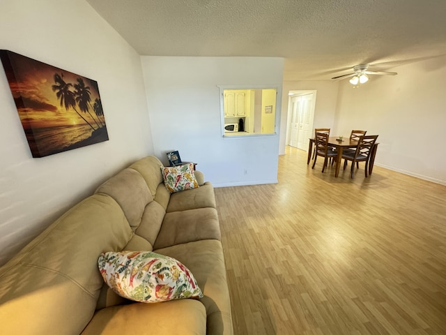 living room with ceiling fan, light hardwood / wood-style flooring, and a textured ceiling