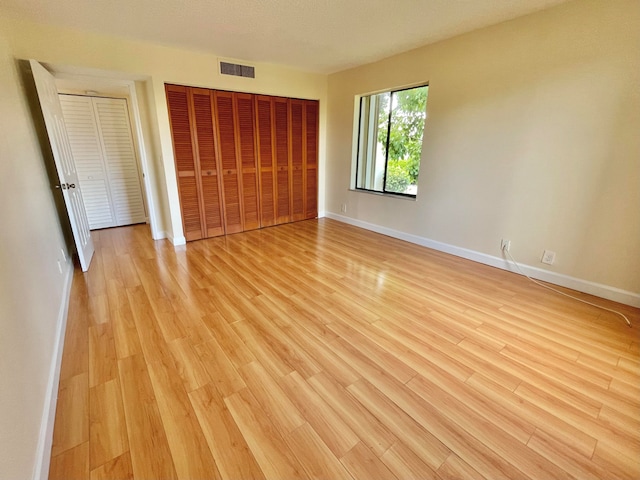 unfurnished bedroom featuring light wood-type flooring, a textured ceiling, and multiple closets