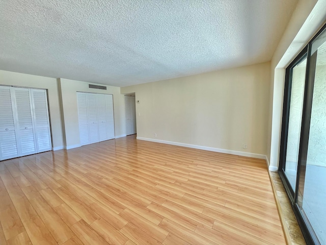 unfurnished bedroom featuring two closets, a textured ceiling, and light hardwood / wood-style flooring