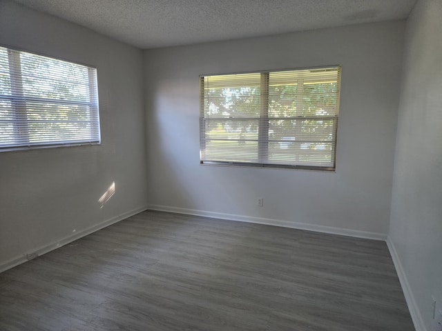 empty room with a textured ceiling, dark hardwood / wood-style floors, and a wealth of natural light