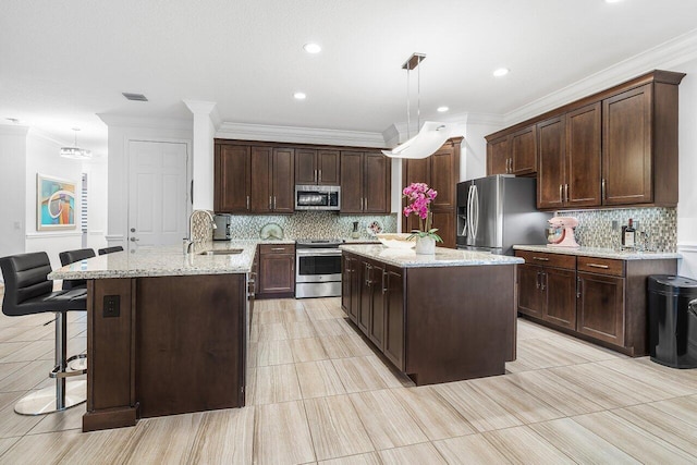 kitchen featuring a kitchen island with sink, hanging light fixtures, stainless steel appliances, and sink