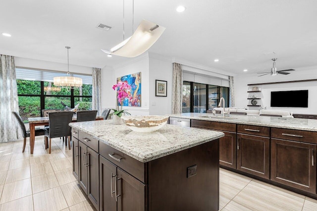 kitchen featuring pendant lighting, a center island, ceiling fan with notable chandelier, sink, and dark brown cabinetry