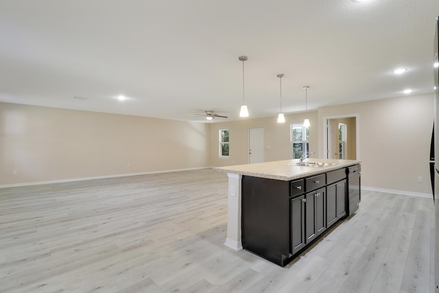 kitchen with pendant lighting, light hardwood / wood-style floors, stainless steel dishwasher, and an island with sink