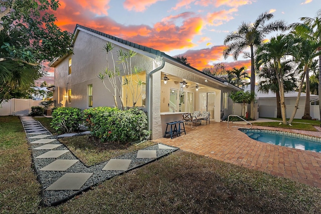 pool at dusk featuring ceiling fan, a patio area, and exterior bar