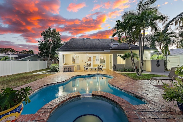 pool at dusk featuring a patio area, an in ground hot tub, and a bar