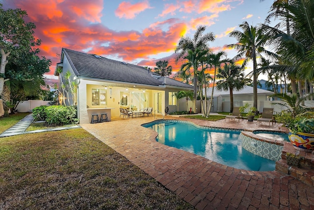 pool at dusk with an in ground hot tub, a bar, and a patio