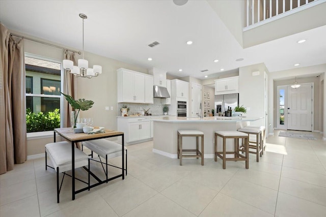 kitchen featuring white cabinets, an island with sink, appliances with stainless steel finishes, tasteful backsplash, and decorative light fixtures